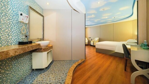 Una habitación de hotel con baño, cama, escritorio y un mural en el techo.