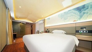 Una habitación de hotel con una cama grande, suelo de madera, televisor montado en la pared e iluminación empotrada en el techo.