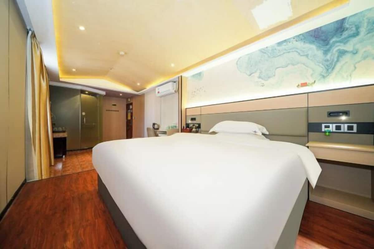 Hotelkamer met een groot bed, een houten vloer, een aan de muur bevestigde televisie en een plafond met inbouwspots.