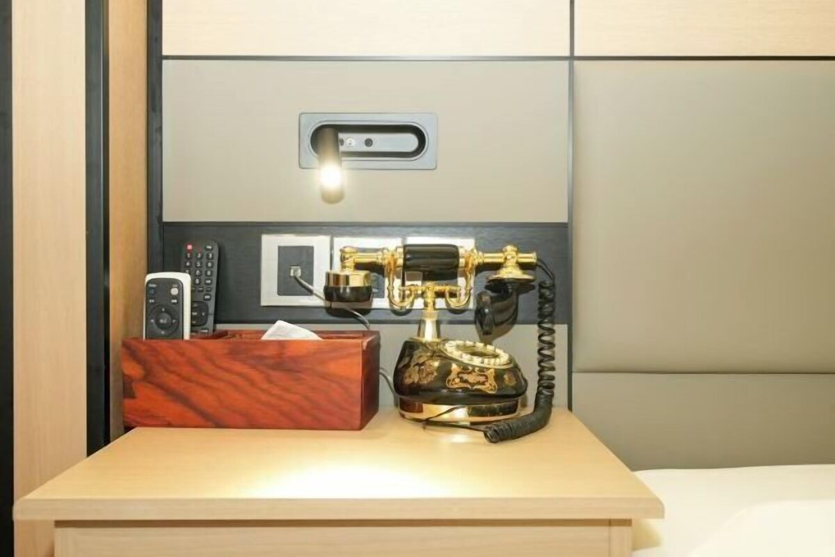 Une table de chevet avec un téléphone, une boîte de mouchoirs et des télécommandes.