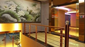 Un vestíbulo de hotel con un gran mural floral, un ascensor de cristal y un mostrador de recepción moderno.