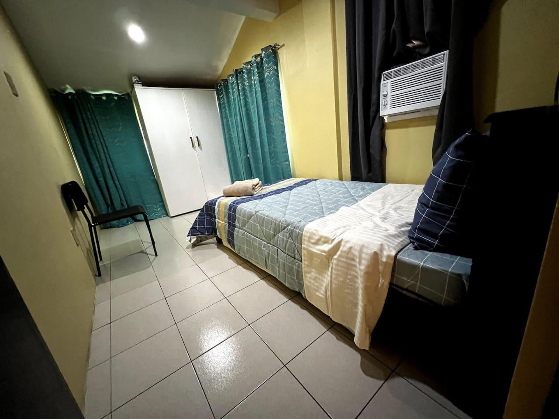 A bedroom with a bed, a chair, a wardrobe, and a window with curtains.