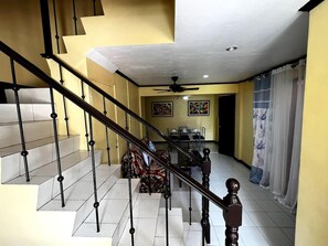 A staircase with black balusters leading to a dining area with a ceiling fan and artwork on the walls. - Casa Talisay Sleeps 6 With Garage (Talisay)
