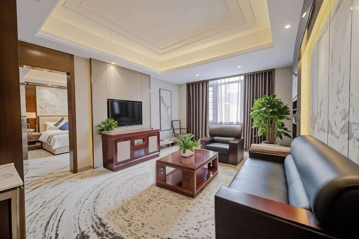 A modern hotel room with a living area, a television, a sofa, a coffee table, and a bed.