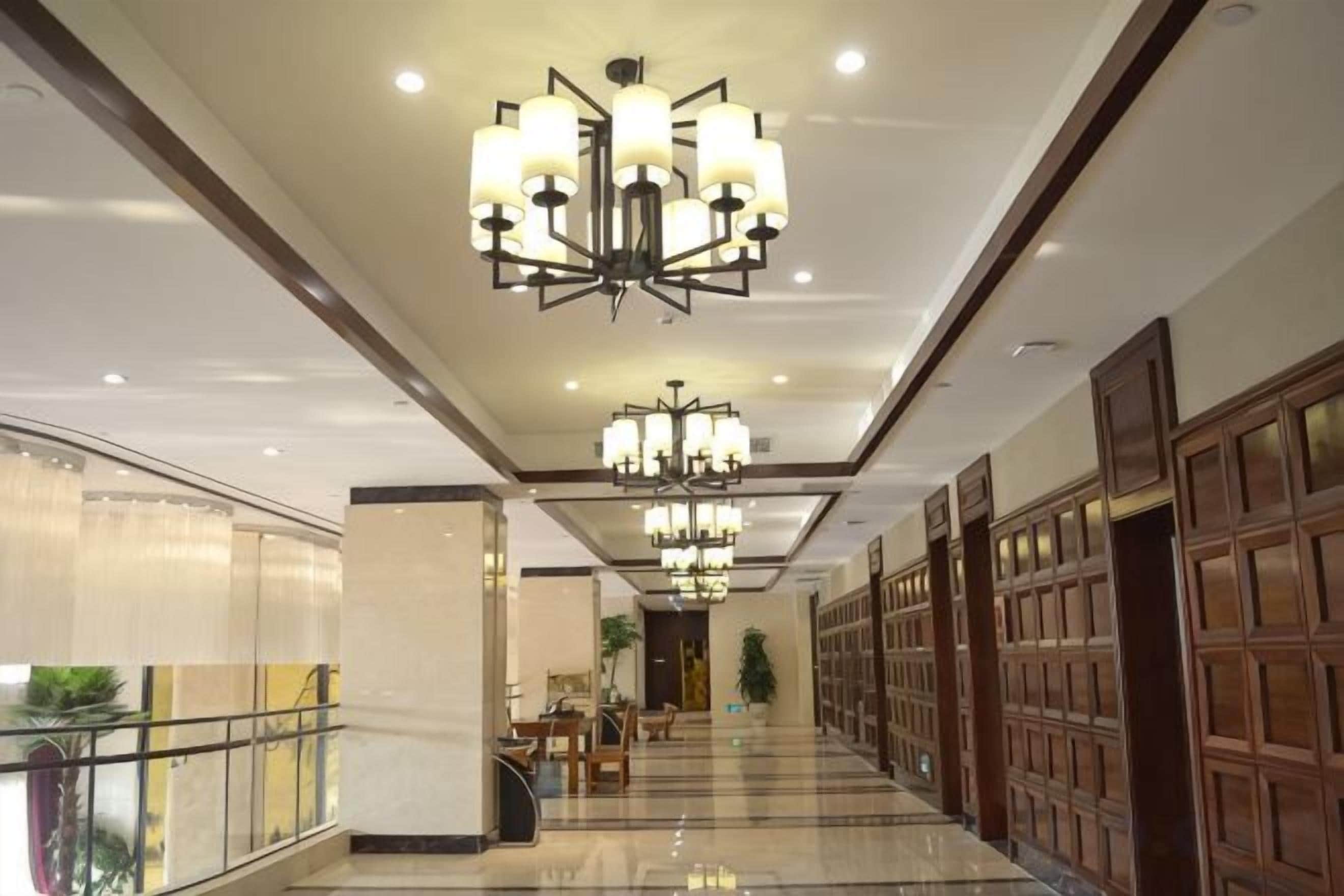 A hotel corridor with chandeliers, a glass railing, and wooden paneling.
