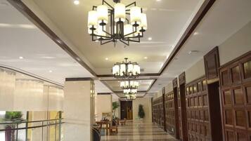 A hotel corridor with chandeliers, a glass railing, and wooden paneling.