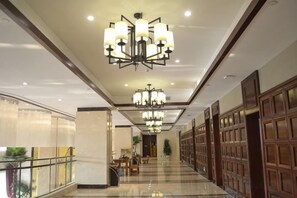 Een hotelgangen met kroonluchters, een glazen balustrade en houten lambrisering.