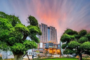 Een hotel met modern design, met een opvallend gebouw met glazen gevel en een verzorgde tuin met diverse bomen.