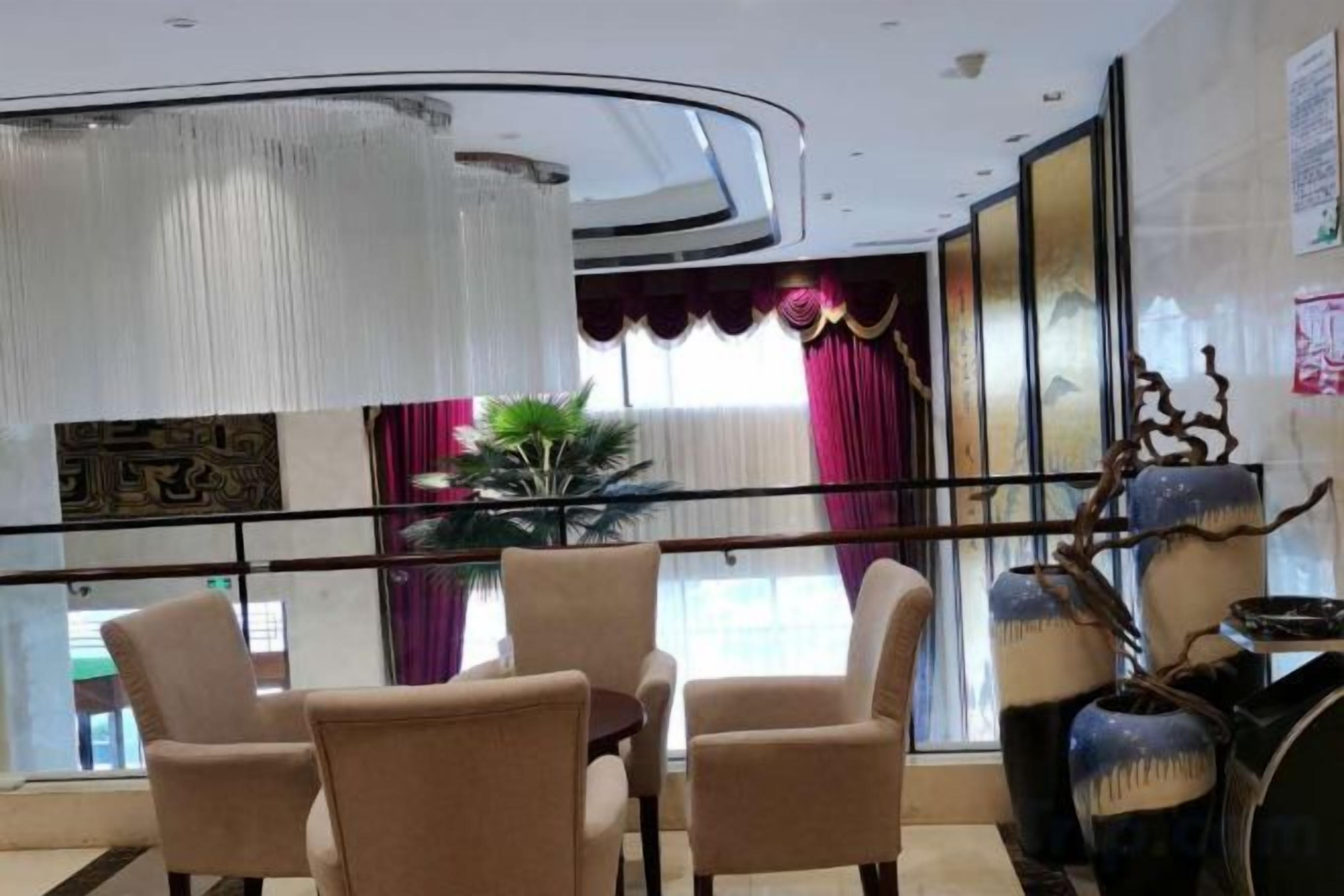 Un hall de hotel con una zona de estar, un amplio ventanal con cortinas y un jarrón decorativo.