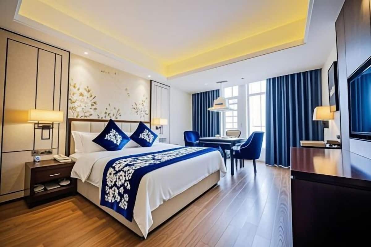 A modern hotel room with a large bed, bedside tables, a desk, and a television.