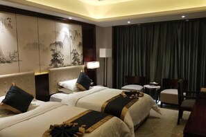 Een hotelkamer met twee bedden, een bureau, een stoel, een lamp en een groot raam met gordijnen.