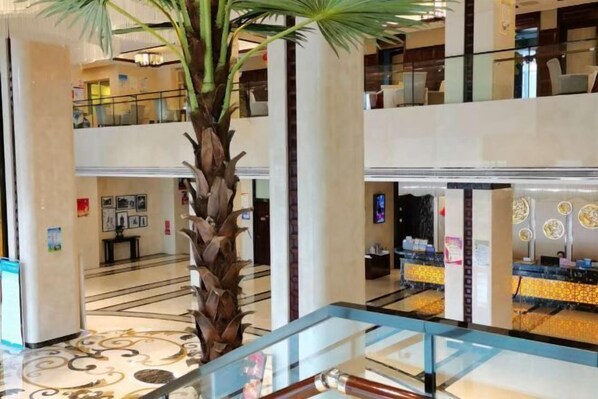 Een meerlaagse hotellobby met een palmboom, een receptiebalie en een glazen balustrade.