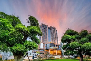 Un hotel moderno con un patio central, rodeado de abundante vegetación y un gran edificio con fachada de vidrio.