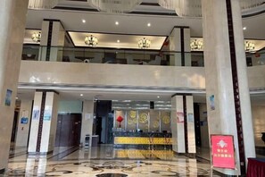 Een hotel lobby met een receptiebalie, een kroonluchter en een rood bord.