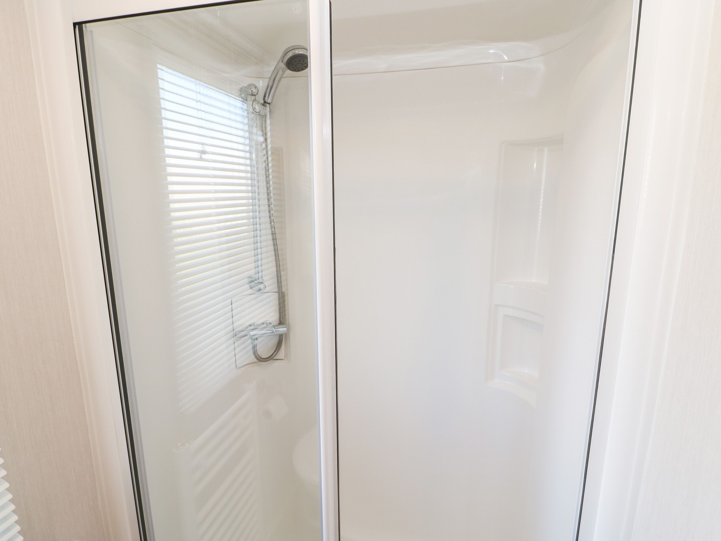 A glass-enclosed shower stall with a handheld showerhead and a control lever.
