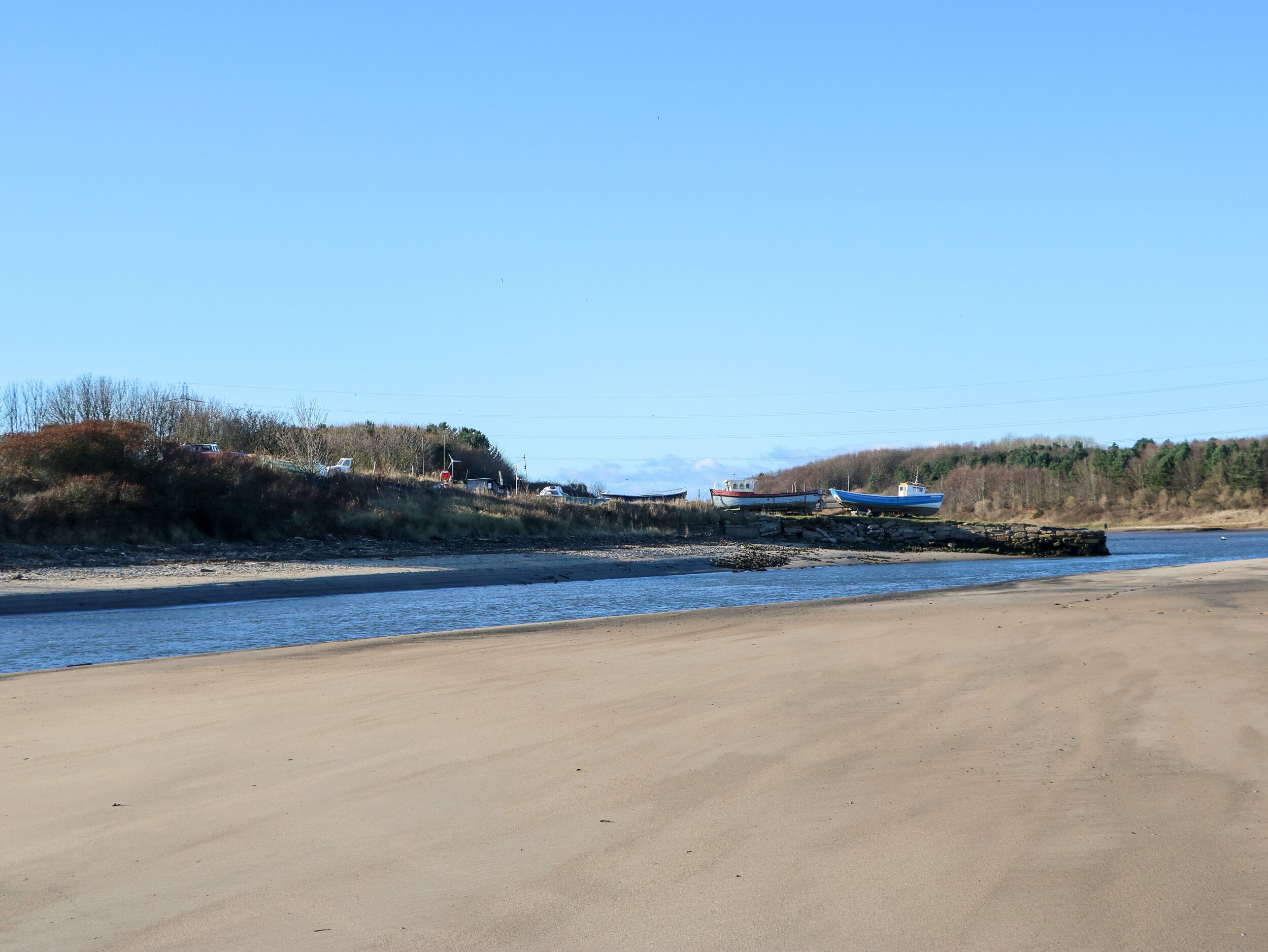 A beach with boats and a stone wall.