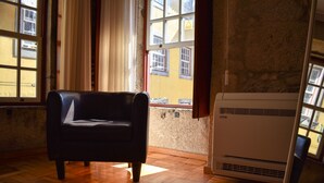 A room with a black leather chair, wooden flooring, a window with curtains, and an air conditioning unit. - Apartamento com 2 Quartos Varanda e Vista rio 3º Andar (Porto)