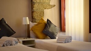 A hotel room with two beds, a nightstand, a lamp, and a wall with a textured design. - Apartamento com 2 Quartos Varanda e Vista rio 3º Andar (Porto)