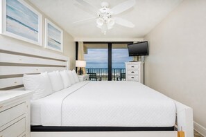 Une chambre d’hôtel équipée d’un lit, d’une télévision, d’un ventilateur de plafond, d’une table de chevet, d’une lampe et offrant une vue sur la plage.