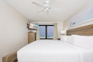 A hotel room with a bed, a ceiling fan, a TV, and a view of the ocean.