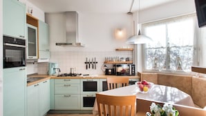 A modern kitchen with light green cabinets, a stove, a microwave, and a dining area with a table and chairs. - 5 minutes from the Alpe di Siusi cable car, family apartment and terrace. (Seis am Schlern)
