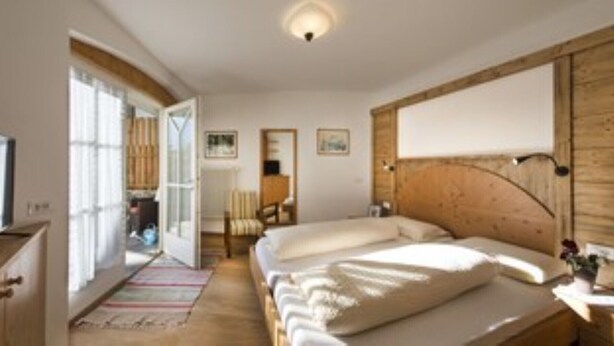 A bedroom with a wooden headboard, a bed with white linens, a chair, and a desk with a lamp. - 5 minutes from the Alpe di Siusi cable car, family apartment and terrace. (Seis am Schlern)