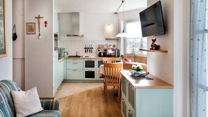 A compact kitchen with light blue cabinets, a wooden dining table, and a TV mounted above it. - 5 minutes from the Alpe di Siusi cable car, family apartment and terrace. (Seis am Schlern)