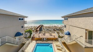 A pool area with a view of the beach, wooden deck, and outdoor seating.