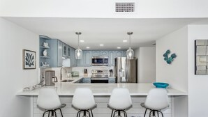 A modern kitchen with white cabinets, a central island with bar stools, and stainless steel appliances.