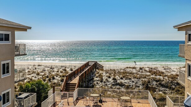 A beachfront property with a wooden deck, outdoor seating, and a view of the ocean.