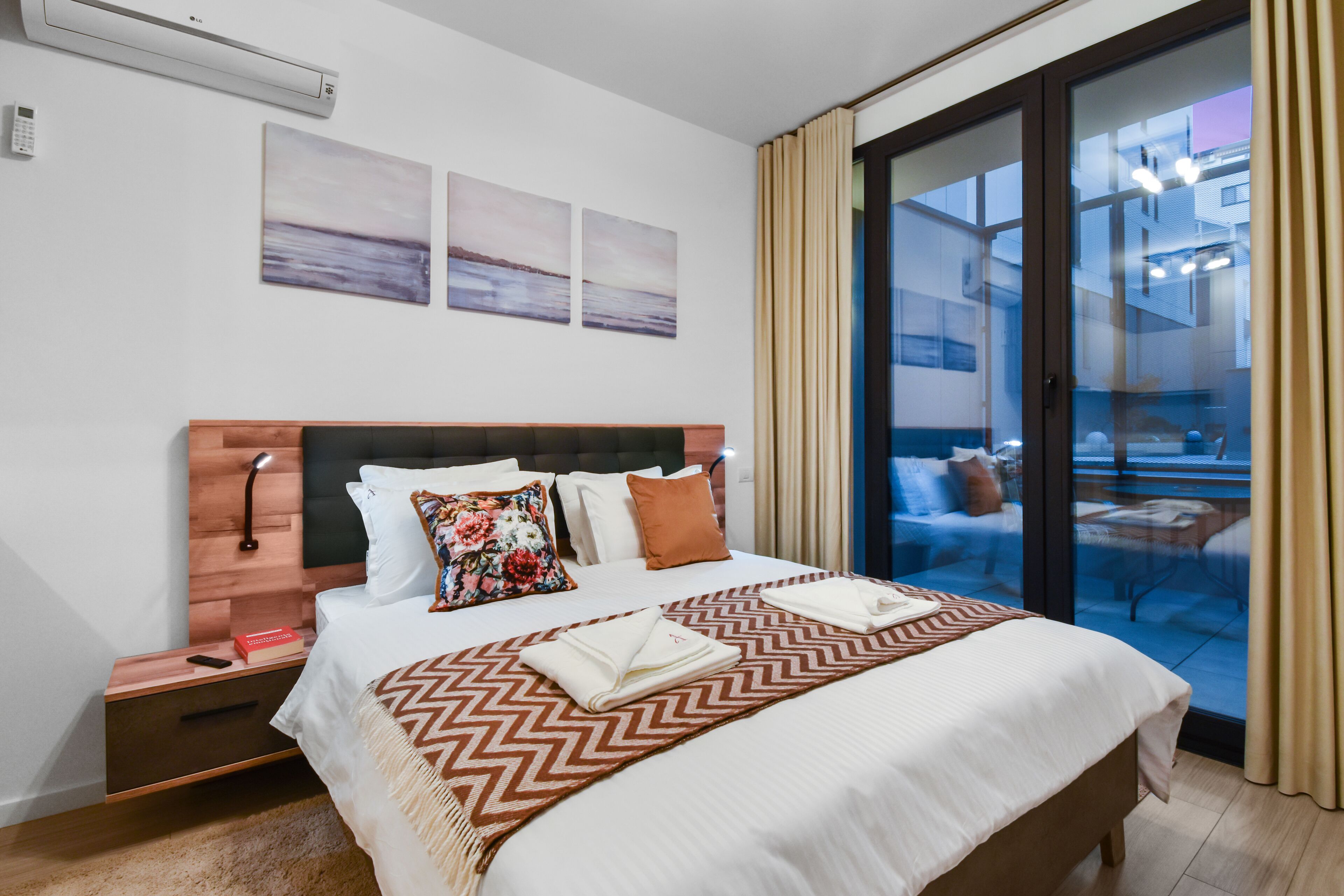 Une chambre d’hôtel comprenant un lit, une table de chevet, un climatiseur fixé au mur et une porte-fenêtre coulissante donnant sur un espace extérieur.