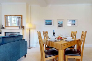 A dining area with a wooden table set for four, a blue sofa, a fireplace, and three framed pictures on the wall. - Rhos Cottage - Two Bedroom Cottage, Sleeps 4 (Conwy)