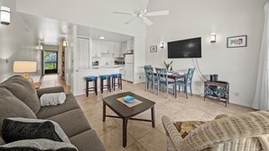 A modern living room with a sofa, a coffee table, and a dining area with chairs and a TV.