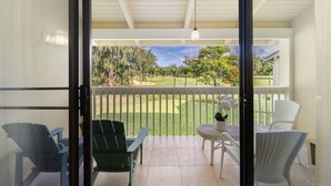 A covered outdoor area with a view of a golf course, featuring a table and chairs.