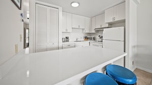 A modern kitchen with white cabinets, a central island with blue barstools, and a refrigerator.