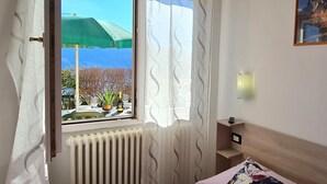 A bedroom with a bed, a window with curtains, a radiator, a nightstand, and a painting on the wall. - Casa Elka Patio 5 Lake view (Tremosine)