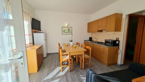 A compact kitchen with wooden cabinets, a dining table with chairs, a refrigerator, a microwave, and a small TV on a stand. - Casa Elka Patio 5 Lake view (Tremosine)