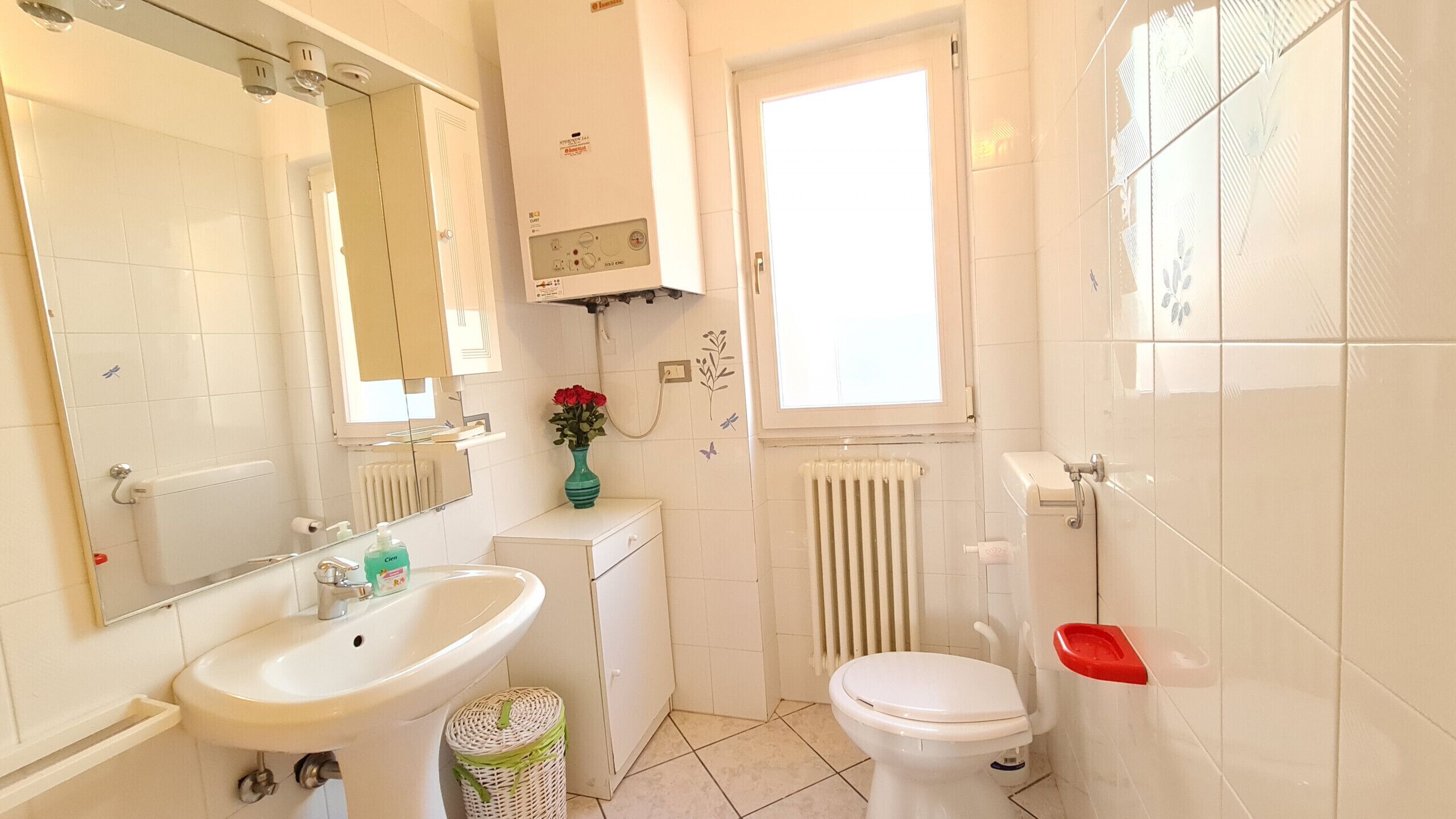 Ein Badezimmer mit weißem Waschbecken, Toilette, Heizkörper und Fenster.