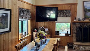 Un comedor con una larga mesa de madera, sillas y un televisor montado en la pared.