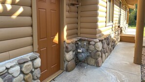 Una cabaña de troncos con base de piedra, una puerta de madera y un porche con pared de piedra.