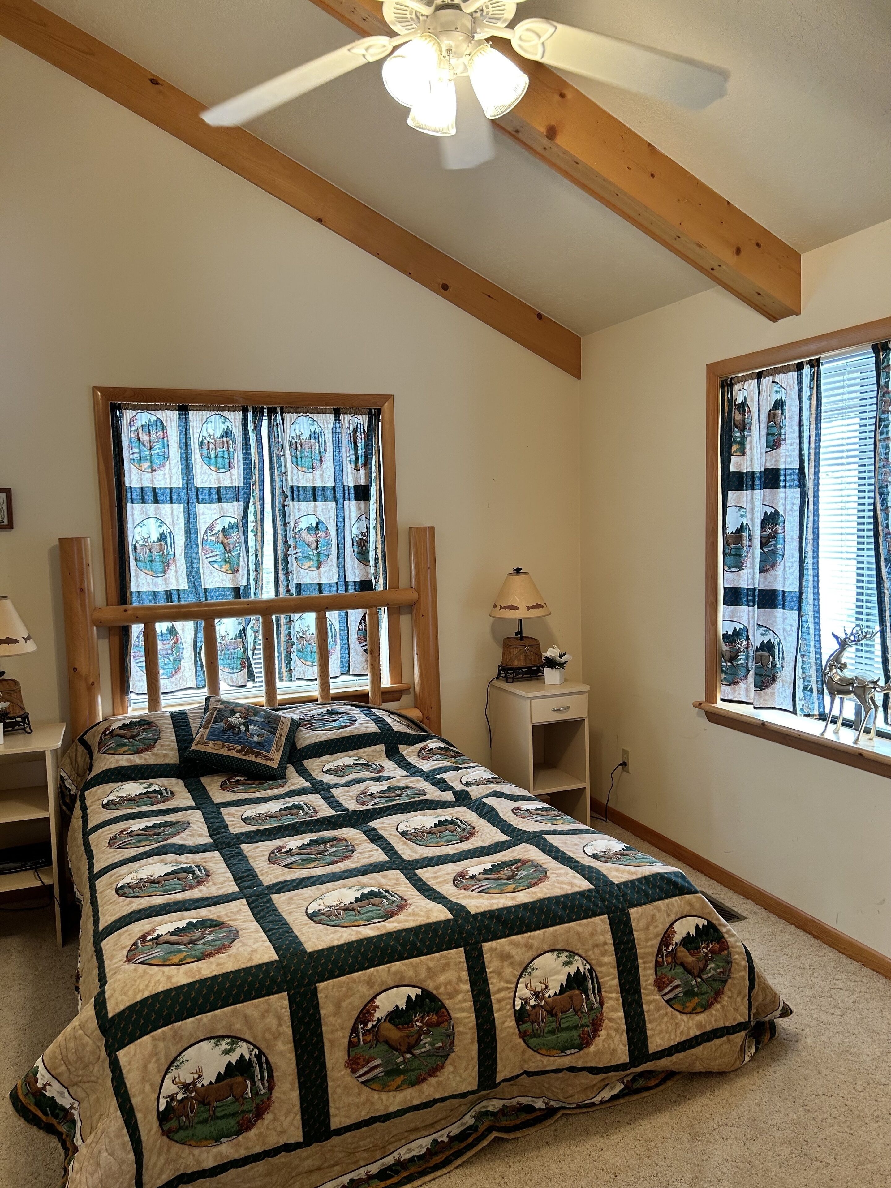 Ein Schlafzimmer mit einem großen Bett, einem Deckenventilator, einem Fenster mit Vorhängen und einem Nachttisch mit Lampe.