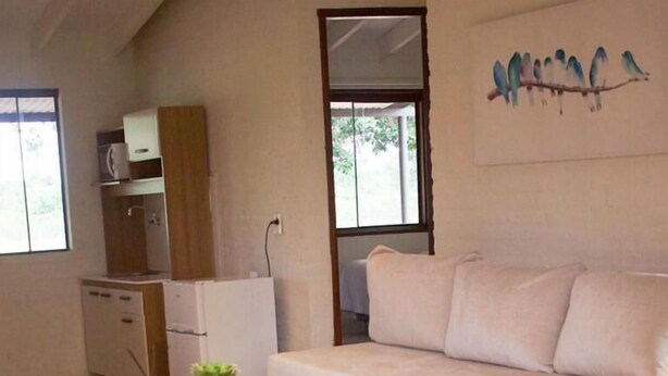 A modern living room with a sofa, a wooden coffee table, and a small side table with a plant. There is a kitchenette area with cabinets and a microwave. - La Matilde Lodge (San Bernardino)