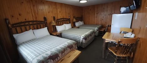 A cabin-style room with two beds, a wooden table, a chair, and a television.