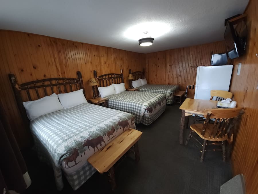 Une chambre de style cabane avec deux lits, une table en bois, une chaise et un téléviseur.