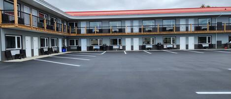 A multi-story hotel with a red roof, multiple balconies, and a parking lot with marked spaces.