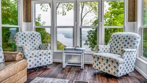 A sunroom with large windows, two patterned armchairs, a small table, and a view of trees and water. - Paradise Point- Sleeps 2 HOT TUB (De Soto)