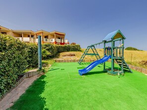 Enjoy a family-friendly stay with a play area featuring a slide and swing set, surrounded by a manicured lawn and hedges.