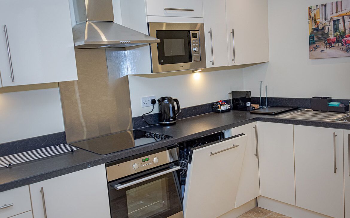 Una cocina moderna con armarios blancos, electrodomésticos de acero inoxidable, una cafetera y un lavavajillas.
