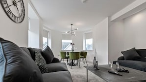 A modern living room with a grey sofa, a coffee table, and a dining area with green chairs. - Mode Winter Garden Apartments (Blackpool)