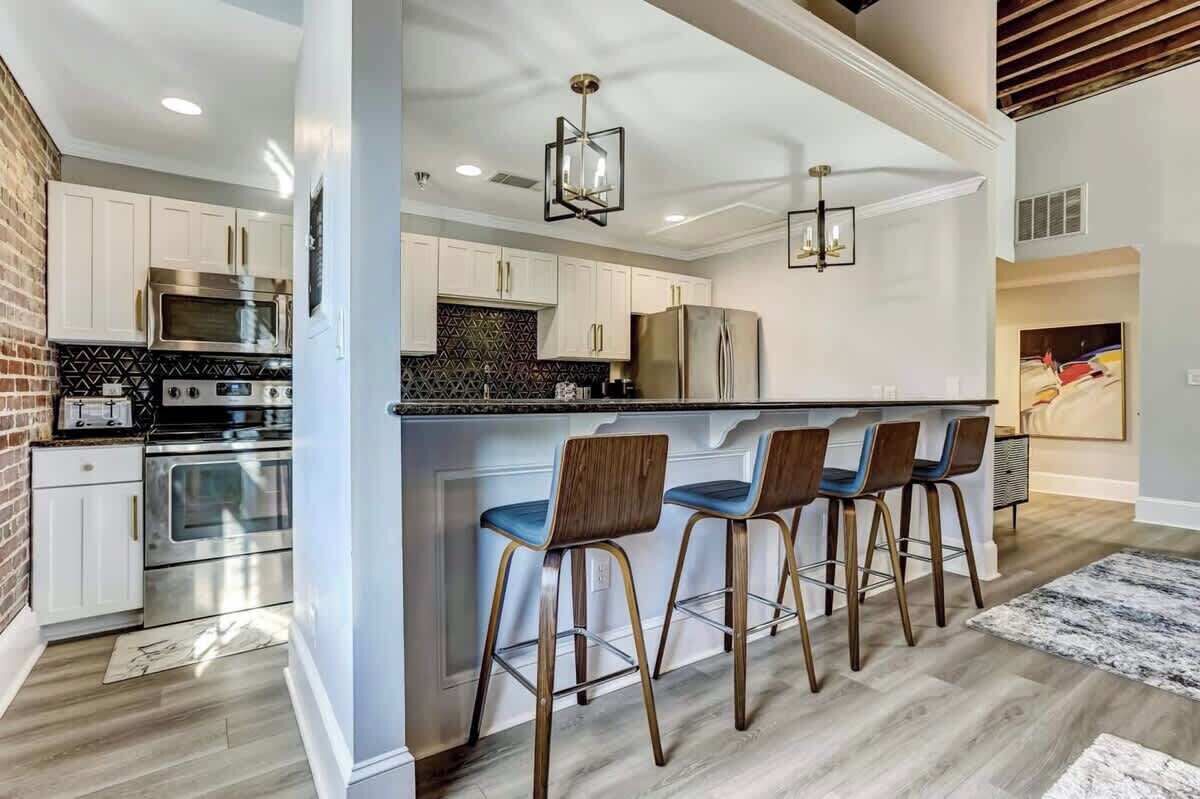 Una cocina moderna con armarios blancos, electrodomésticos de acero inoxidable y una zona de bar con taburetes.